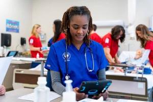 澳门线上赌博平台大学 nursing student in blue scrubs looking at iPad in simulation lab.